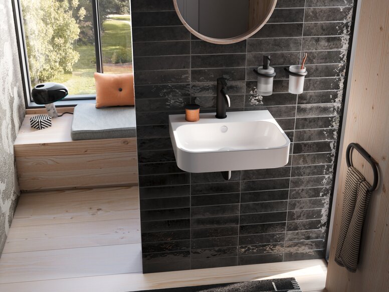 A white washbasin with a black tap and two wall-mounted cups on a black tiled wall in the wash area, set against a backdrop of black tiles