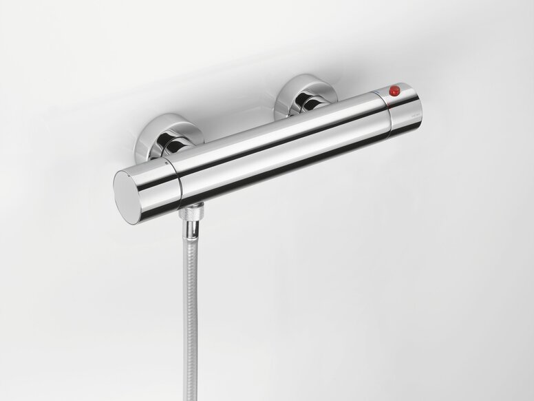 Chrome-plated thermostat with a red knob and a hose connection on the lower left-hand side of a white wall