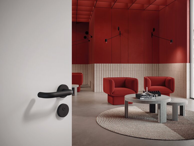 HEWI System 111 lever handle A black door handle with a rosette-shaped escutcheon on a light grey door; behind it, a waiting area with a table and two chairs