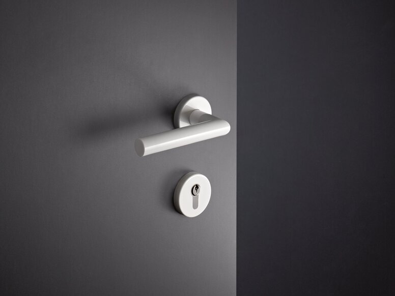 White synthetic material door handle with a round rosette and a lockable key cylinder, fitted to a grey door