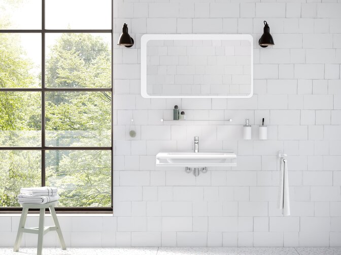 A washbasin with a side-mounted towel holder beneath a rectangular mirror with integrated lighting in the wash area, set against a white tiled wall