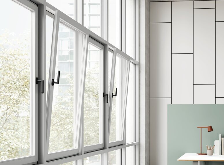 Four black window handles on adjacent tilt-and-turn windows in an office