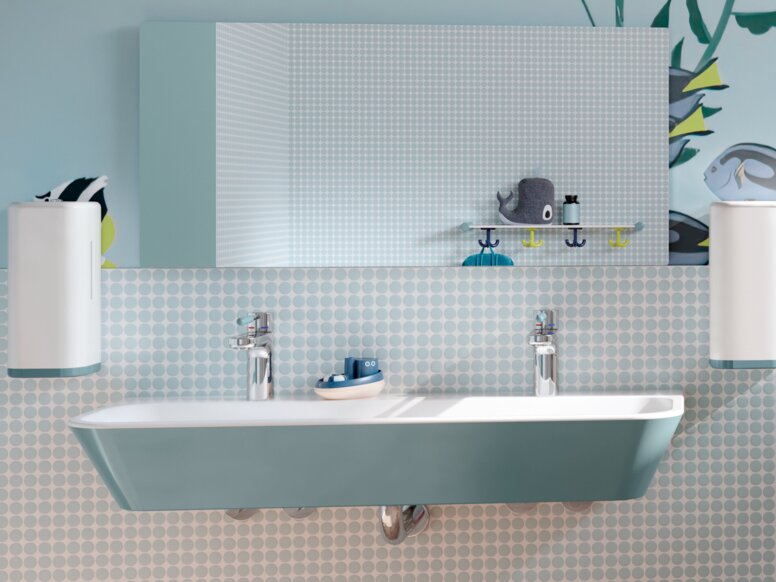 HEWI Serie 801 ICONIC Interieur Blauer Kinderwaschtisch aus Mineralguss mit Seifenspendern und einem Spiegel darüber, daneben ein WC-Bereich