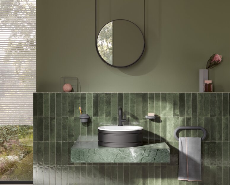HEWI Serie 477 Interieur Rundes Waschbecken auf grünem Marmorwaschtisch mit schwarzem Wasserhahn und Handtuchhalter, darüber ein runder Spiegel