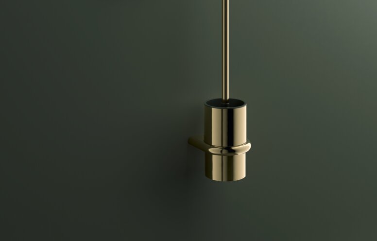 Wall-mounted toilet brush and toilet roll holder with a brass-coloured PVD coating on a dark green wall