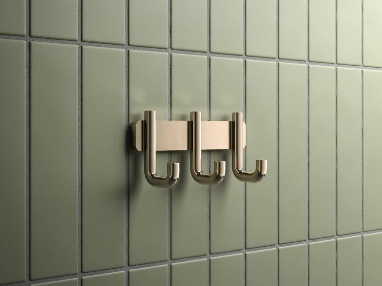 HEWI Range 480 PVD hook rail Triple hook rail with a brass-coloured PVD coating against a backdrop of green tiles