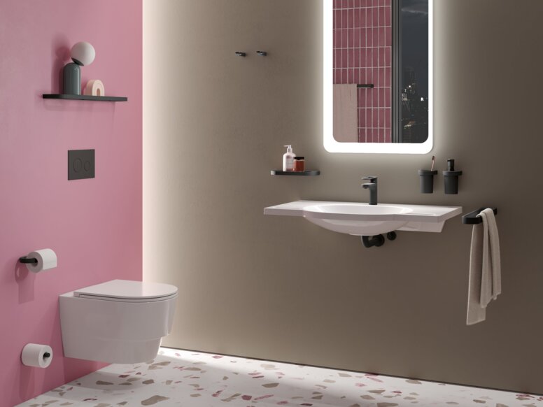 Wandhängendes WC mit geschlossenem Deckel, daneben Waschbecken mit Handtuchhalter, zwei Becherhaltern und beleuchtetem Spiegel