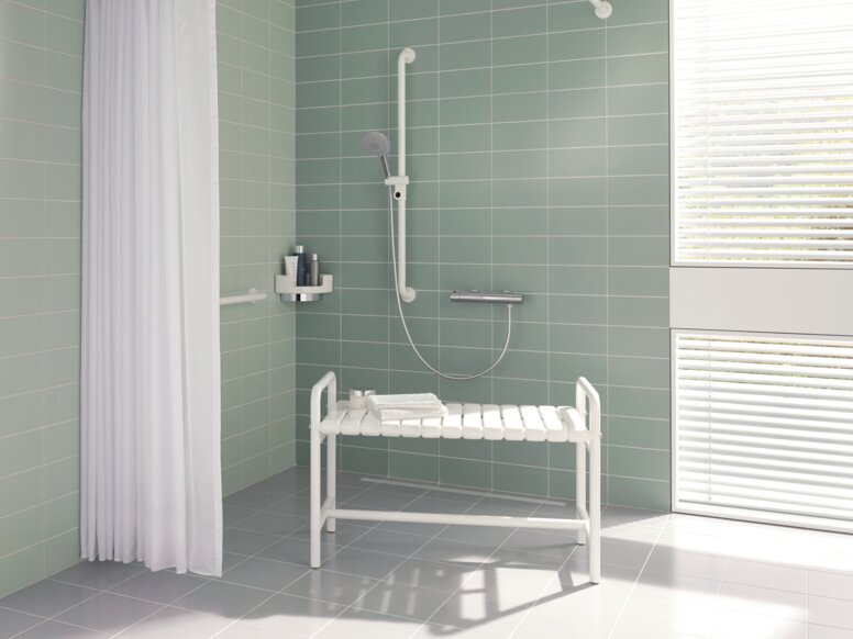 White shower bench with armrests and a shelf in the shower area against a light green tiled wall