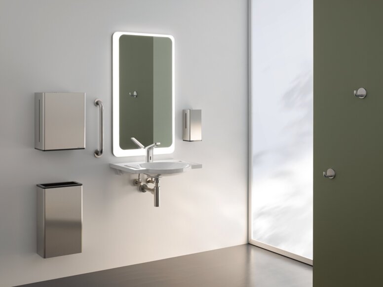 A lighted mirror, with a washbasin underneath, complete with a paper towel dispenser and a waste bin, against a white wall