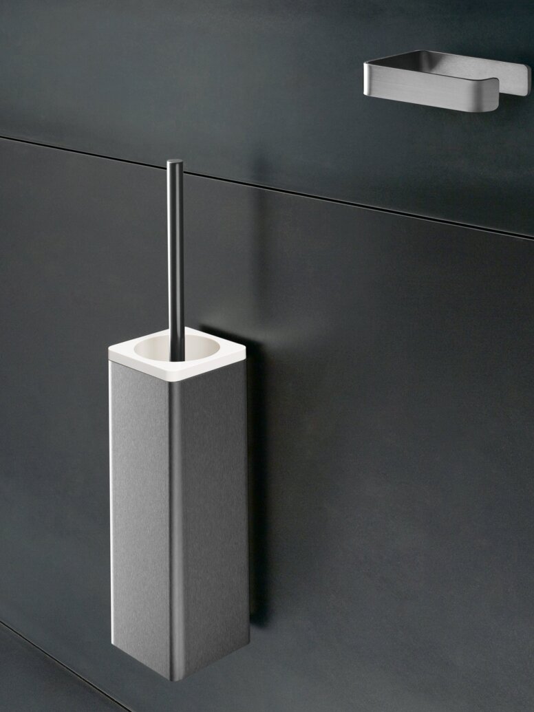 Stainless steel toilet brush unit with a rectangular container and brush handle on a dark grey wall, beneath a small wall bracket
