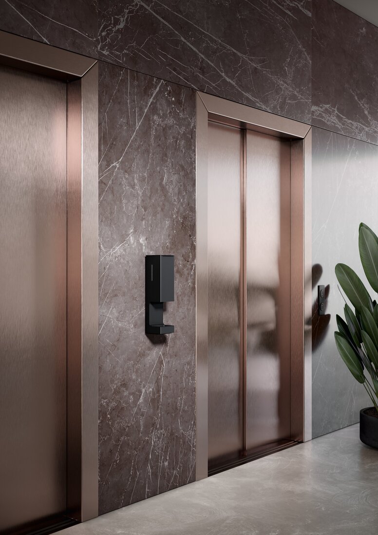 Black powder-coated disinfectant dispenser installed next to two lift doors