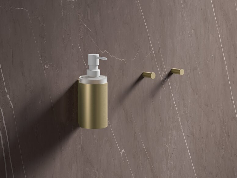 Brass-coloured PVD soap dispenser attached to a brown marble wall with two hooks