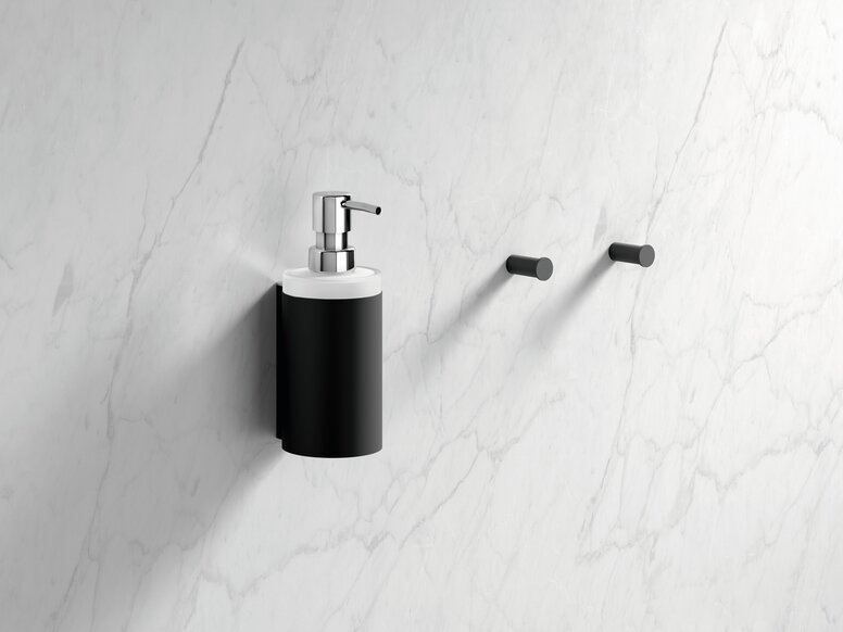 Black powder-coated wall-mounted soap dispenser with a lever pump and two hooks, set against a white marble background