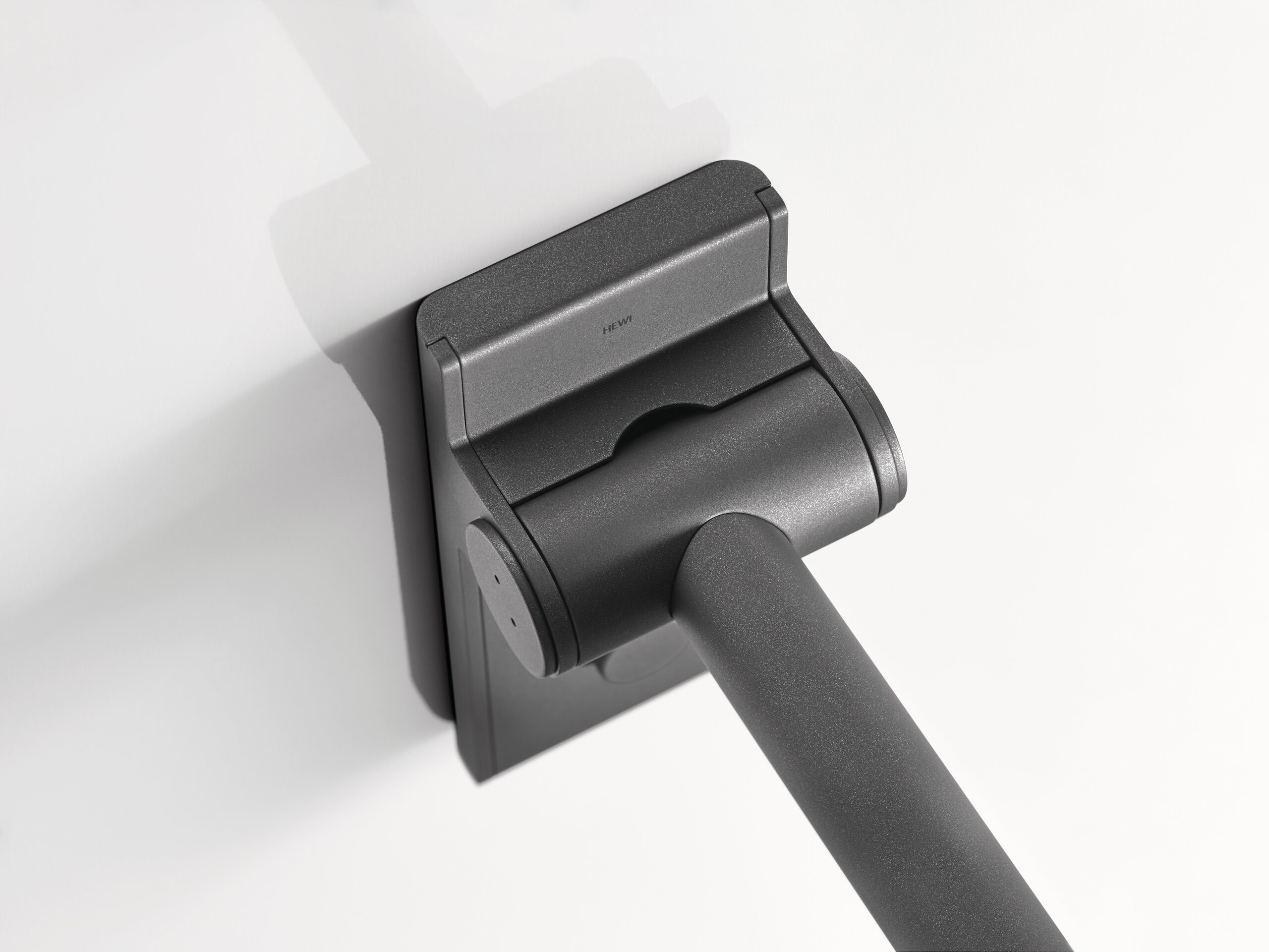 Close-up of the matt black hinge section of a Mono hinged support rail with a rectangular wall mounting plate and a rail extending diagonally downwards
