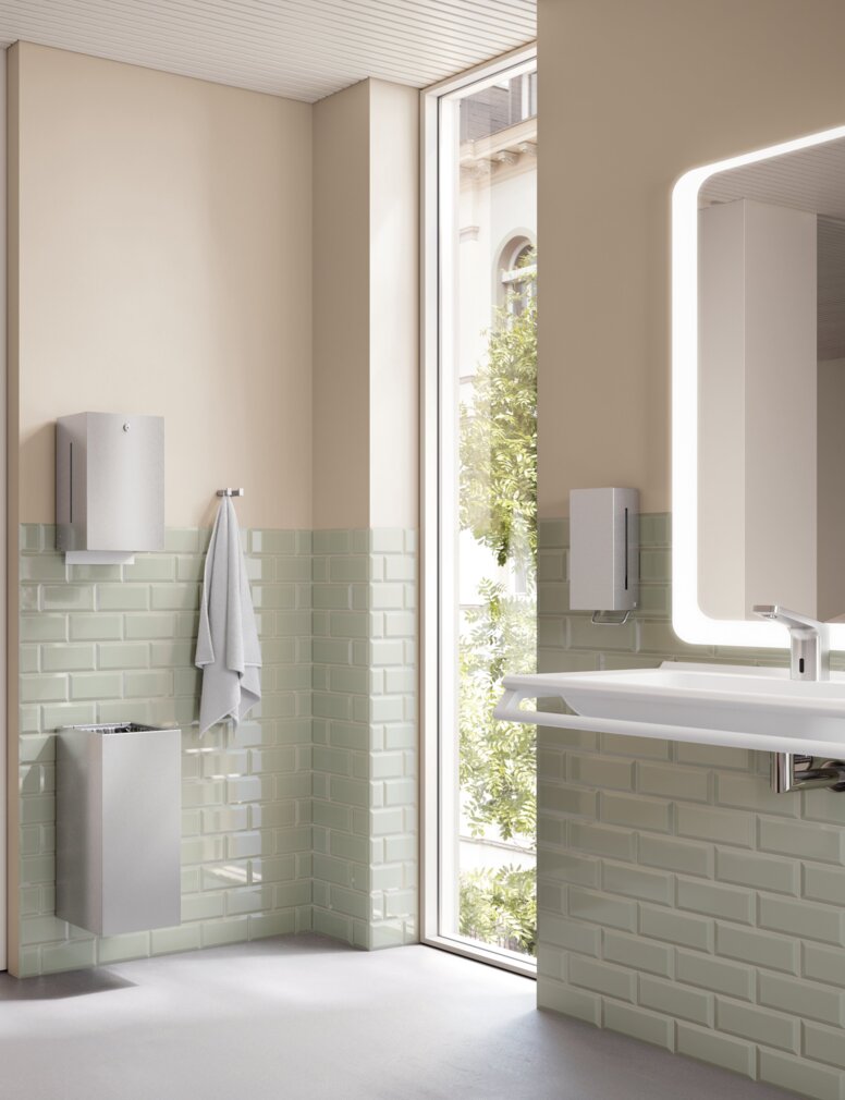 HEWI System 900Q Interieur WC mit WC-Papierhalter, Haltegriff und Toilettenbürste im Bad mit hellgrünen Fliesen und beigefarbener Wand