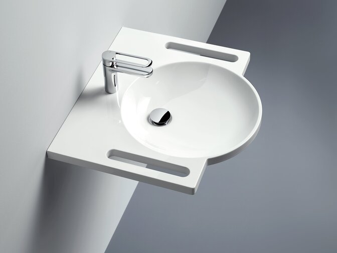Wall-mounted round washbasin made of mineral composite with integrated handles on both sides and a tap against a light grey wall