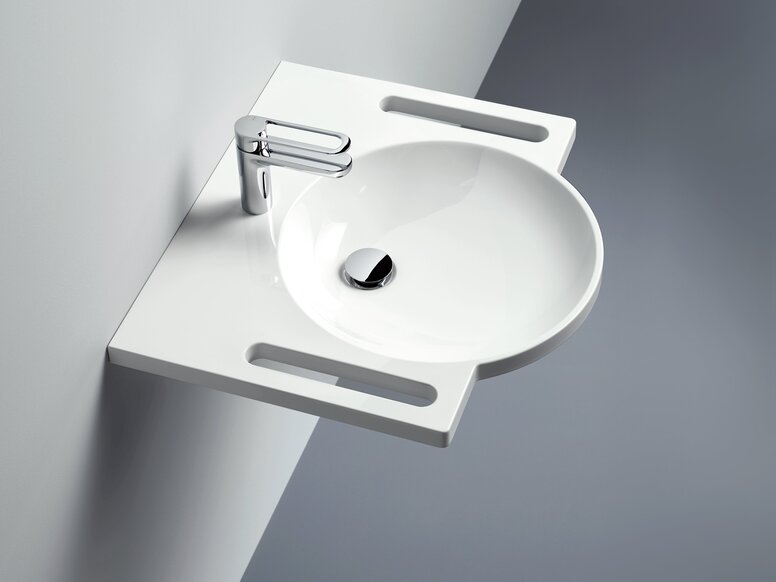 Wall-mounted round washbasin made of mineral composite with integrated handles on both sides and a tap against a light grey wall