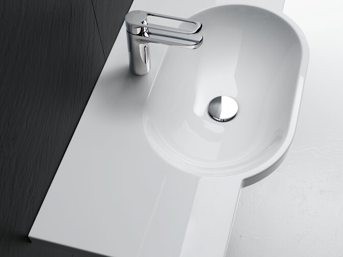 White mineral composite washbasin with an oval basin, side shelf and tap set against a dark grey wooden surface