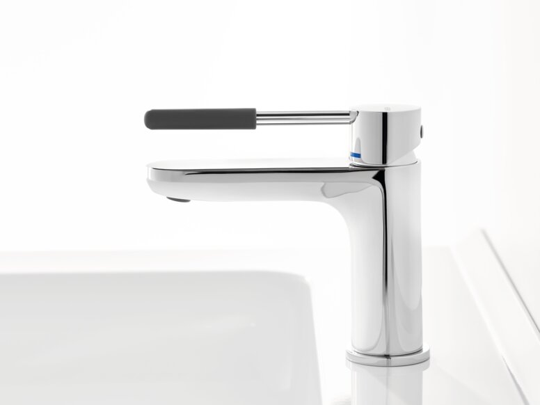 HEWI AQ single-lever washbasin mixer tap Chrome-plated tap with a long lever handle and dark grey grip sleeve on a white washbasin against a white background