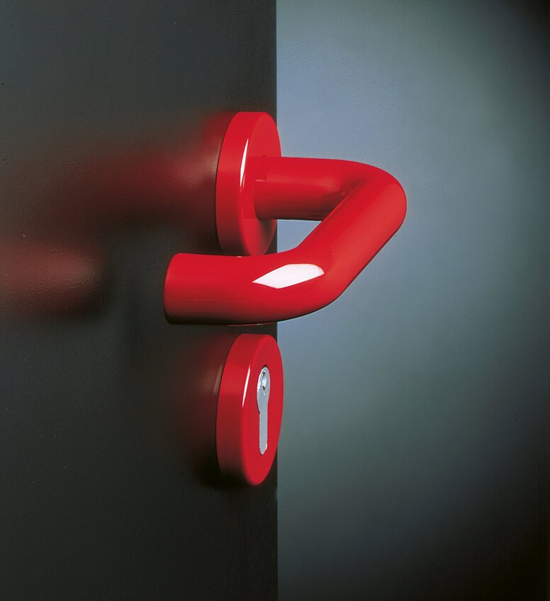HEWI System 111 Door Handle Red door handle with an angled lever and round rose on a dark door, with a second round escutcheon featuring a narrow opening below