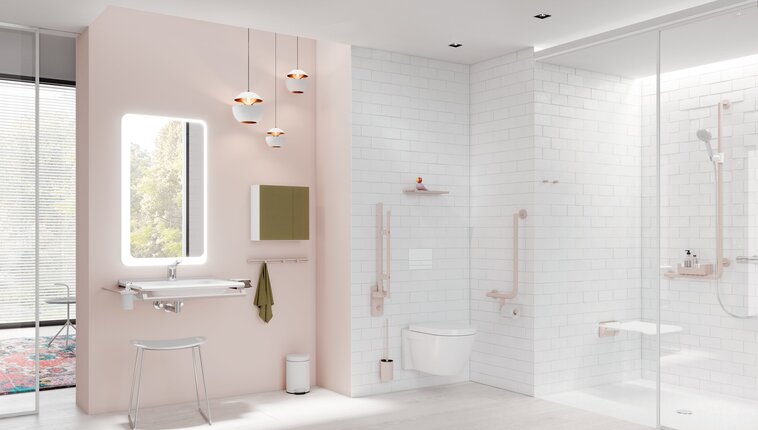 Bright bathroom with a pale pink feature wall, illuminated mirror above a white washbasin, wall-hung toilet and level-access shower with white wall tiles and light-coloured grab rails