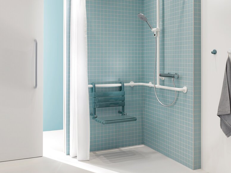 Shower area of a patient bathroom in blue and white with a view through a sliding door